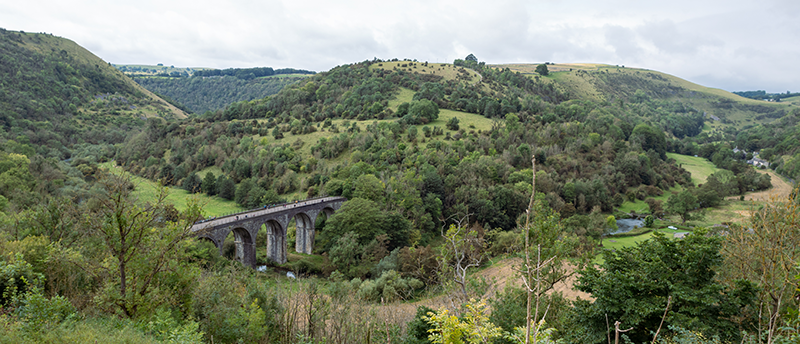 View of the Monsal head bridge. Placed in a long turning river valley with green hills.